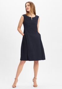 Navyblaues ärmelloses Kleid mit einem Schlüsselloch-Ausschnitt, seitlichen Taschen und einem ausgestellten Saum. Hergestellt aus glattem Stoff mit einem schlichten Design.