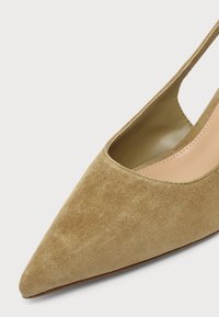 Μπεζ δερμάτινο παπούτσι slingback με μυτερή μύτη από σουέτ και λείο ταμπά εσωτερικό φόδρα σε ανοιχτό φόντο.