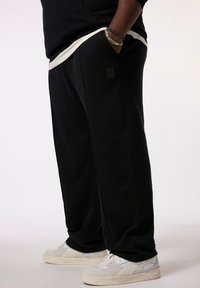 Sorte sweatpants med en afslappet pasform, sidelommer og et lille logo-patch. Bæres med off-white sneakers med grå detaljer.