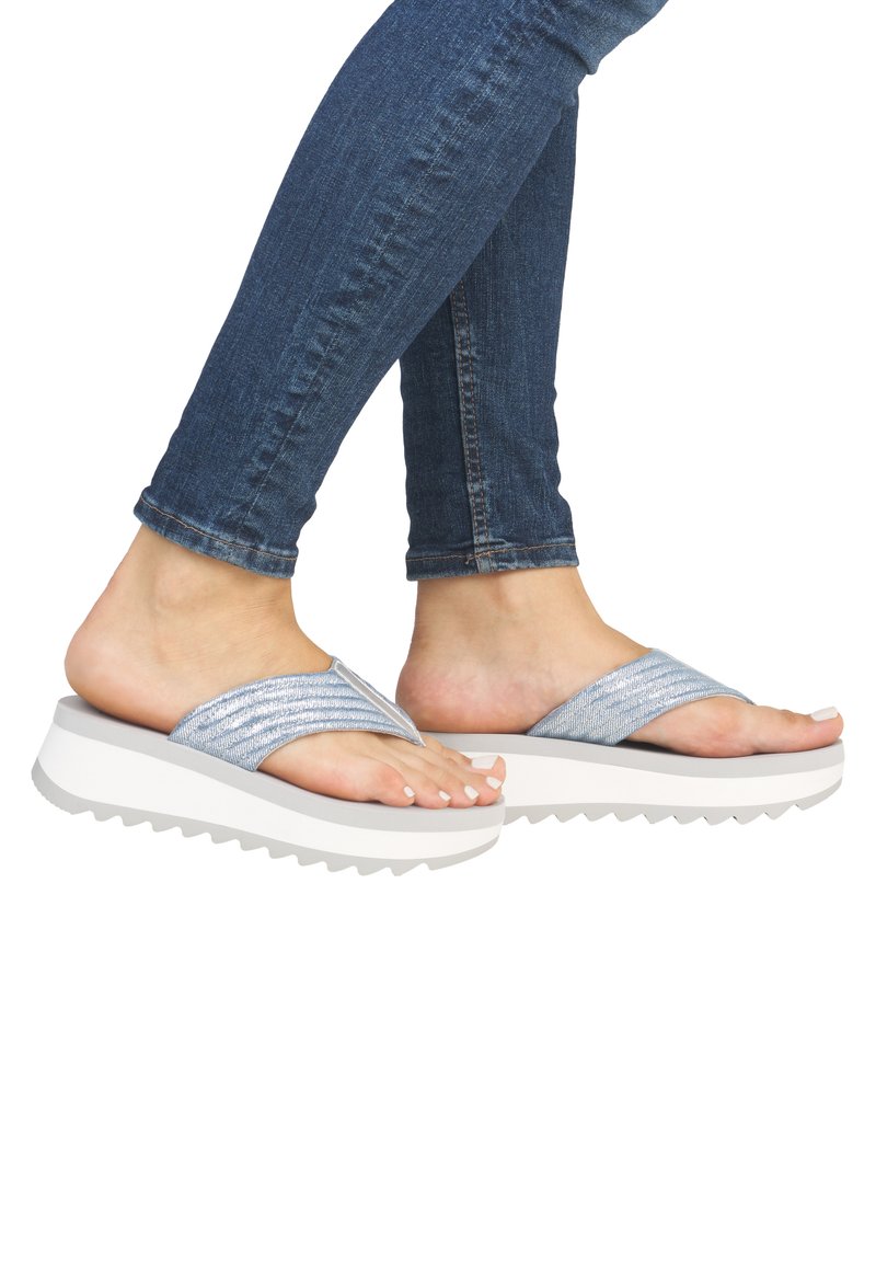 Des tongs plateforme avec des sangles métalliques bleues, une semelle épaisse blanche, une texture en zigzag et une finition lisse. Portées avec un jean longueur cheville.