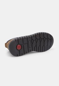 Pantof cu piele maro, având o talpă din cauciuc negru, cu un model texturat de tracțiune și un accent circular roșu aproape de toc.