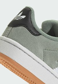 Zelené semišové tenisky s čiernou koženou pätnou časťou, bielou textúrovanou medzipodrážkou a oranžovou gumovou podrážkou. Na päte a na boku je umiestnené logo.