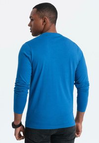 Langarm-T-Shirt aus leuchtend blauer Baumwolle, enganliegendes Design, glatte Textur, Rundhalsausschnitt und gesäumte Säume, kombiniert mit schwarzen Jeans.