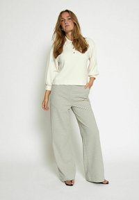Cream pullover with a polo collar and three buttons, paired with wide-leg striped pants in black and white. Smooth fabric, relaxed fit.