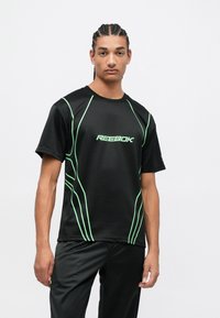 Čierne atletické tričko s zelenými akcentovými líniami a logom "Reebok" na prednej strane. Krátke rukávy a hladká, tkanina absorbujúca vlhkosť.