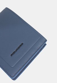 Cartera de cuero azul con una textura lisa, forma rectangular y un acento de logo negro con costuras azules en contraste.