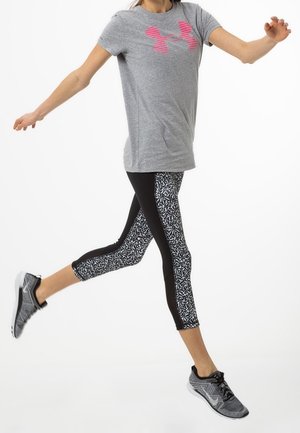 Grijze t-shirt met korte mouwen met een roze logo. Zwarte leggings met witte abstracte patronen en een aansluitend ontwerp. Zwarte sportschoenen.