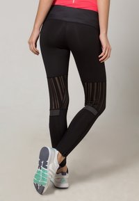 Czarne legginsy sportowe z wysokim stanem i siateczkowymi wstawkami z pionowymi paskami. Połączone z białymi sneakersami z zielonymi akcentami.