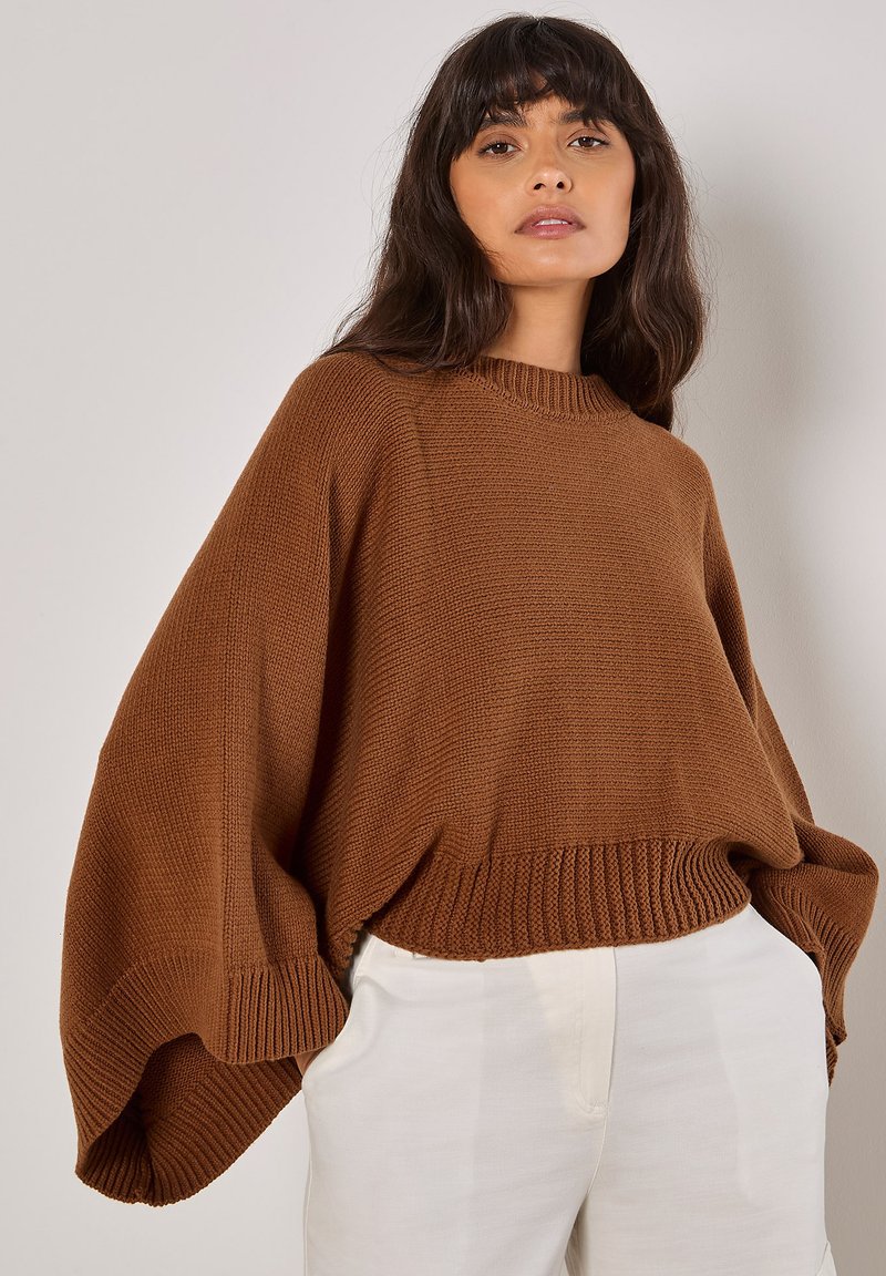 Brauner, gestrickter Pullover mit weiten Ärmeln und geripptem Saum. Verfügt über einen Rundhalsausschnitt und ein strukturiertes Muster, kombiniert mit hellen Hosen.