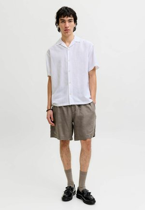 Wit linnen overhemd met korte mouwen en knoopsluiting, gecombineerd met losse beige korte broek. Gestyled met zwarte schoenen en lichtbruine sokken.