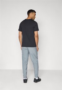 Zwarte katoenen t-shirt gecombineerd met lichtgrijze sportbroek, voorzien van zijzakken en zwarte accenten, gedragen met zwarte sportschoenen.
