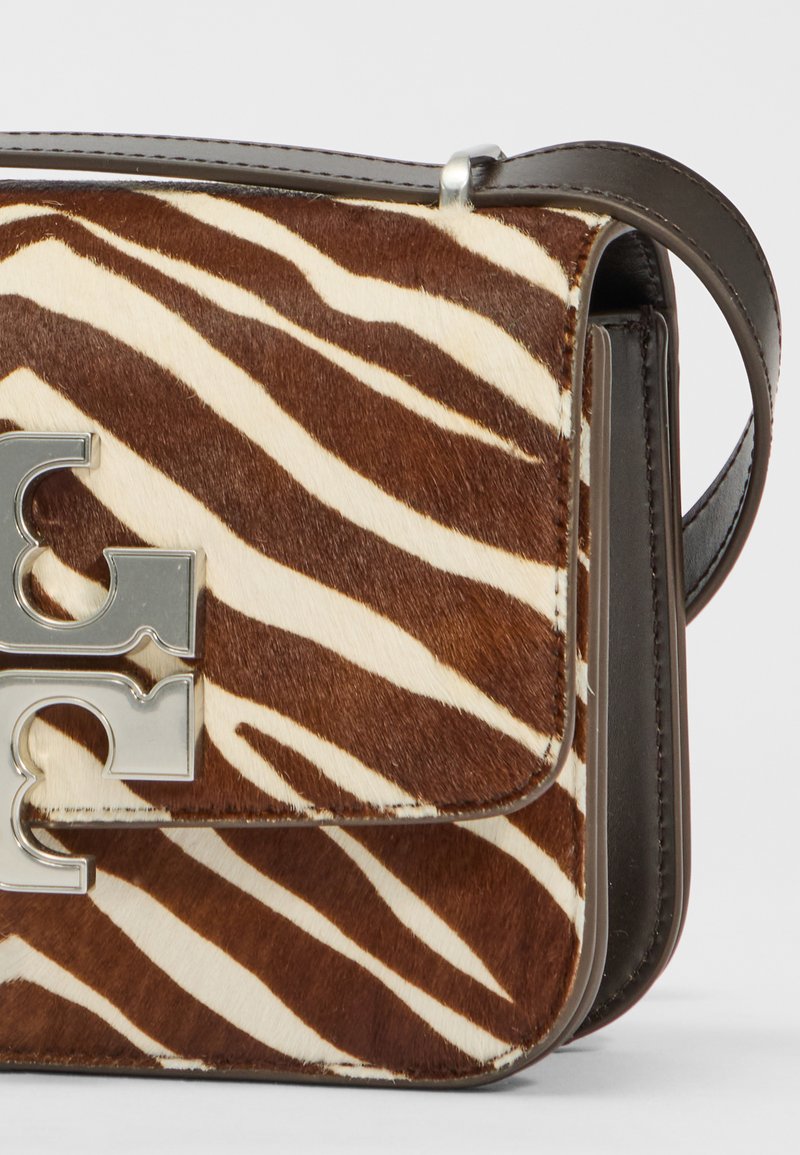 Brązowa i kremowa torebka w paski zebra o gładkiej fakturze, z akcentem w postaci srebrnego logo i ciemną skórzaną rączką.