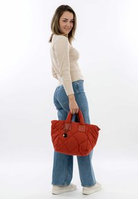 Borsa a tracolla rosso trapuntata con due manici e un charm decorativo. La borsa ha una consistenza morbida e una forma quadrata, adatta per un uso casual.