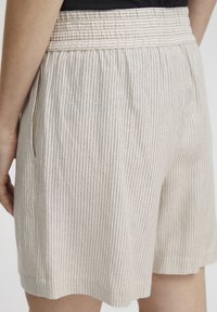 Pantalones cortos a rayas beige hechos de una tela ligera. Cuentan con una cintura elástica, bolsillos laterales y un corte relajado con un dobladillo ligeramente festoneado.