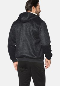 Black hoodie with a textured, speckled finish. Features a hood, ribbed cuffs and hem, and is paired with dark pants.