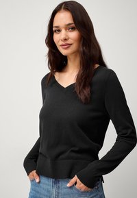 Maglione nero a maglia con scollo a V e polsini a costine. Presenta un design aderente e un orlo leggermente accorciato, abbinato a denim blu.