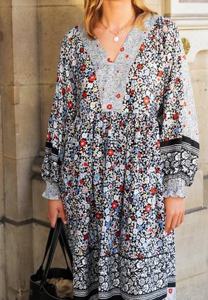 Sukienka w kwiatowy wzór z czarnym tłem i kolorowymi kwiatami, z dekoltem w kształcie litery V oraz bufiastymi rękawami, w połączeniu z czarną torebką.
