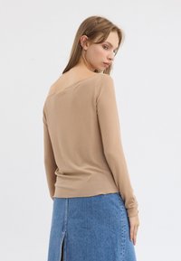 Beige rillede langermet topp med bred av-høyden nakkesnitt, supplert med en lett tilpasset fasong og myk tekstur.