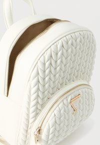 Zaino in ecopelle bianca con texture intrecciata, dotato di due scomparti con zip e un dettaglio logo a triangolo in tono oro.