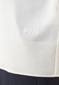 Maglione bianco lavorato a maglia con orlo e colletto a coste, caratterizzato da un sottile logo "BOSS" impresso sul petto. Texture liscia.