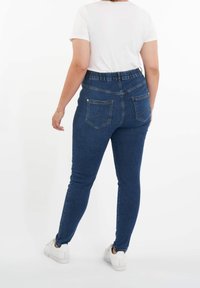 Siniset farkut, joissa on kapea malli ja korkea vyötärö, sekä kaksi takataskua. Yhdistetty yksinkertaiseen valkoiseen t-paitaan ja valkoisiin lenkkarikenkiin.