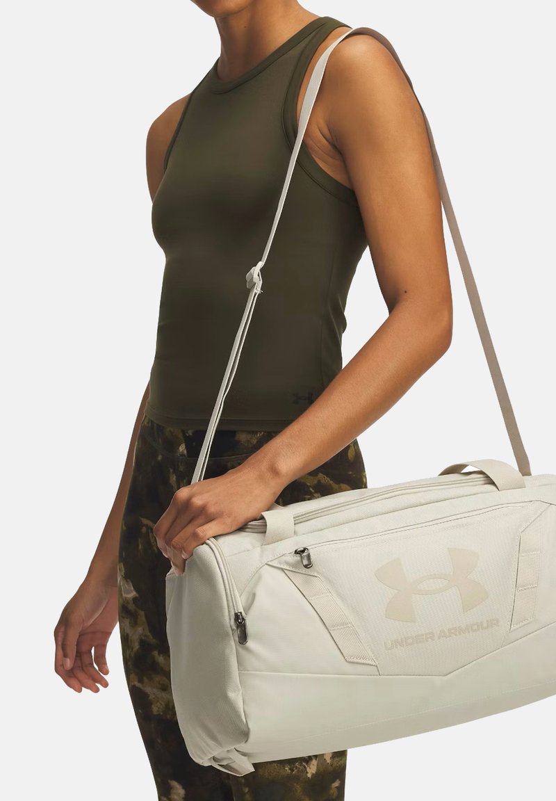 Borsa a cilindro bianca con superficie testurizzata, presenta un grande logo Under Armour. Cinghia grigia regolabile, cerniere laterali per uno stoccaggio sicuro.