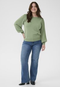 Lysegrøn strikket sweater med ribstrikkede ballonsærmer, kombineret med blå vidde jeans og sorte ankelstøvler. Glat tekstur, afslappet pasform.