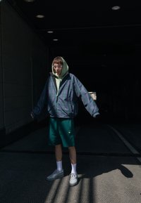 Överdimensionerad rutjacka i blått, grönt och lila, bärs över en mintgrön hoodie, tillsammans med gröna shorts och grå sneakers.