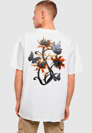 Weißes Baumwoll-T-Shirt mit einem grafischen Aufdruck von Blumen und Schmetterlingen in den Farben Orange, Schwarz und Grau, ergänzt durch goldene Schrift.