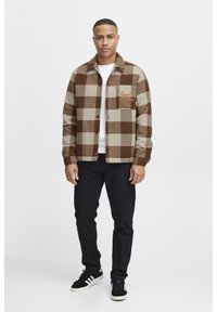 Brown and beige plaid jacket in wool blend, featuring a front pocket with "Good Vibes" embroidery, black jeans, and sneakers.