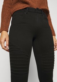 Svarta jeans med en skräddarsydd design och ribbade detaljer på låren. Tyget har en slät textur och en klassisk femficksstil.