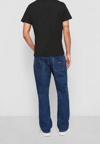 Camiseta negra de manga corta combinada con jeans de mezclilla azules, con un corte recto y bolsillos traseros, llevada con zapatillas blancas.