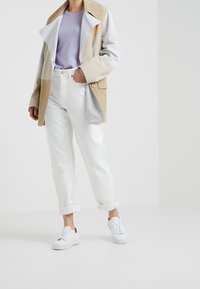 Manteau en daim bicolore beige, gris clair et crème ; associé à un jean blanc retroussé et des baskets blanches. Look décontracté.