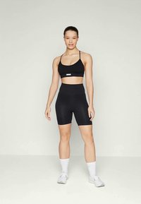 Crni atletski crop top s tankim naramenicama, uparen s crnim kratkim hlačama visokog struka koje imaju vertikalnu rebrastu teksturu. Bijele tenisice i čarape do gležnja.