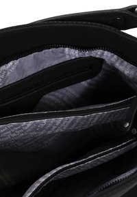 Schwarze Handtasche innen mit mehreren Fächern und Reißverschlüssen. Ausgekleidet mit grauem Stoff, der mit Text bedruckt ist. Glatte Textur.