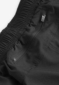 Zwarte sportshorts met een gestructureerde elastische tailleband, een zijzak met rits en een gladde stof met verstevigde stiksels.