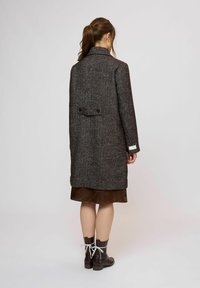 Grå texturerad ullkappa med öppning bak, knappar och en skräddarsydd krage, bärs över en brun satin klänning och bruna stövlar.