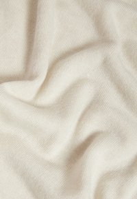 Tissu tricoté doux de couleur crème avec une texture visible et des plis doux créant une surface lisse et confortable.