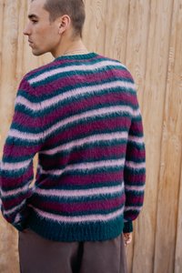 Striped knitted sweater in shades of dark green, purple, and pink. Soft, fuzzy texture with a crew neckline and ribbed hem.