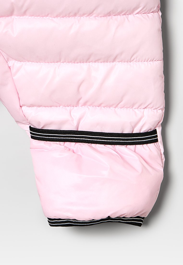 Manga de chaqueta acolchada de color rosa claro con diseño acolchado. Presenta un puño elástico de rayas negras y blancas texturizadas en el extremo.