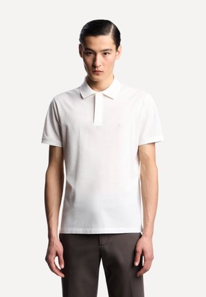 Polo bianco realizzato in cotone texturizzato, con patta e maniche corte. Presenta un logo discreto sul petto e un design classico.