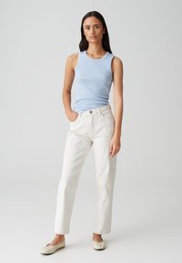 Top in cotone ribbed di un azzurro chiaro abbinato a pantaloni bianchi a vita alta. Il modello indossa delle semplici scarpe flat color crema. Design semplice e pulito con accenti minimi.