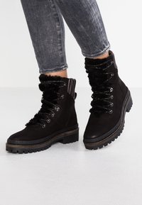 Botas de tobillo de ante negro con ribete de pelo sintético, ojales de metal y suelas de goma gruesas, que presentan un frente con cordones texturizados.