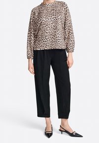 Top s leopardím vzorem v béžové a černé barvě, spárovaný s černými tapered kalhotami a černými slingback podpatky s špičatými špičkami.