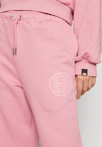 Pantalones de chándal rosa claro fabricados con mezcla de algodón; cuentan con cintura elástica, impresión de logo en la pierna y detalles de costura tonal.