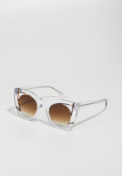 Lunettes de soleil avec monture transparente et verres dégradés marron. Design angulaire en chat, avec un motif écaille de tortue subtil en haut.