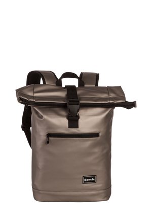 Sac à dos gris à rabat fabriqué en matériau imperméable, avec une poche zippée à l'avant, du matériel noir et des bretelles ajustables pour le confort.