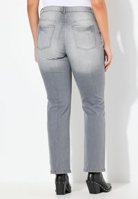 Jeans grigi, slim-fit, con una texture sbiadita, dotati di due tasche posteriori e cuciture dettagliate, abbinati a stivaletti neri con tacco.