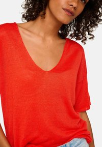 Bright red, short-sleeve, lightweight sweater with a deep V-neckline. Soft texture and relaxed fit, featuring slightly rolled sleeve hems.
