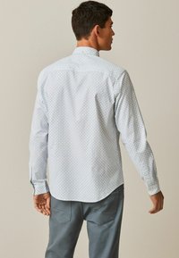 Langærmet skjorte i lyseblå med geometrisk mønster, knap-ned krave og buet kant. Stoffet ser glat ud med en blød tekstur.